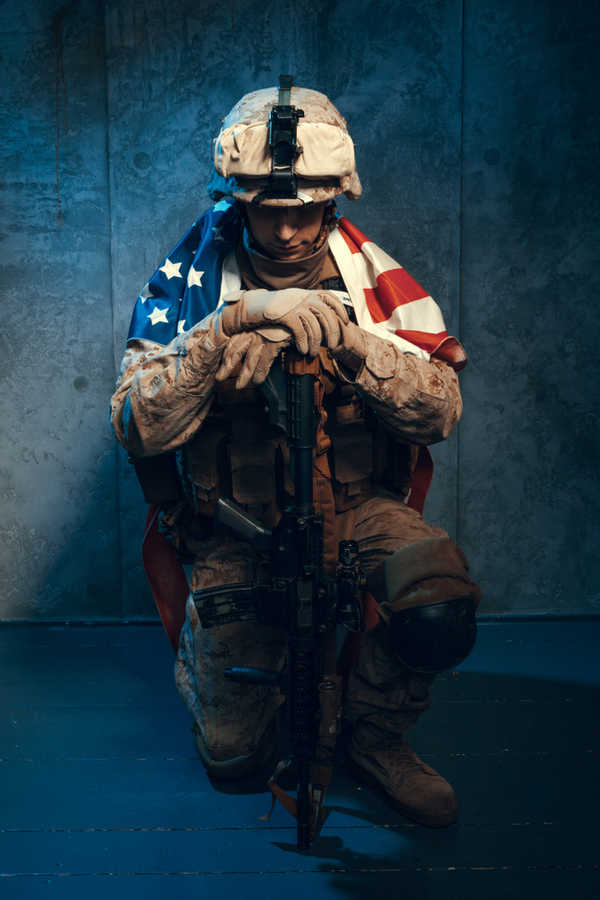 military soldier kneeling with US Flag over shoulders
